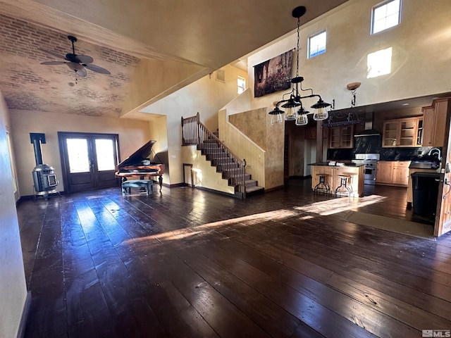 interior space with dark wood-type flooring, ceiling fan with notable chandelier, a wood stove, a high ceiling, and sink