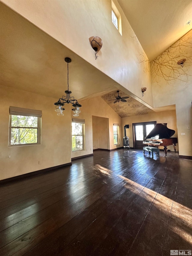 unfurnished living room featuring ceiling fan with notable chandelier, dark hardwood / wood-style flooring, high vaulted ceiling, and a wealth of natural light