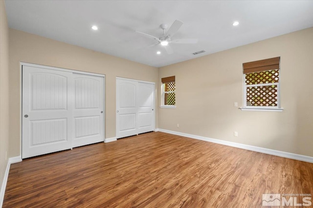 unfurnished bedroom featuring two closets, ceiling fan, and hardwood / wood-style flooring