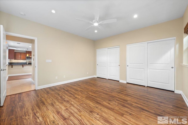 unfurnished bedroom featuring ceiling fan, multiple closets, and dark hardwood / wood-style flooring