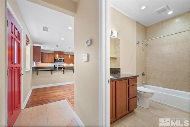 full bathroom featuring wood-type flooring, vanity, tiled shower / bath combo, and toilet