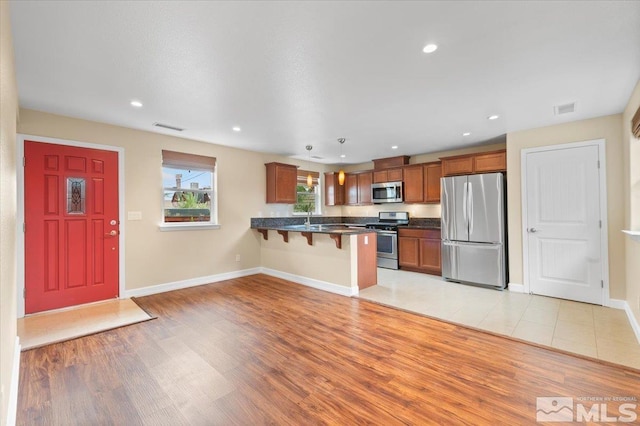 kitchen with light hardwood / wood-style floors, sink, kitchen peninsula, a kitchen breakfast bar, and appliances with stainless steel finishes