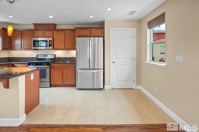 kitchen with dark stone countertops, pendant lighting, a breakfast bar area, and appliances with stainless steel finishes