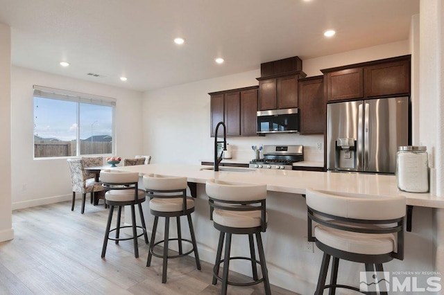 kitchen featuring sink, dark brown cabinets, appliances with stainless steel finishes, light wood-type flooring, and a kitchen bar