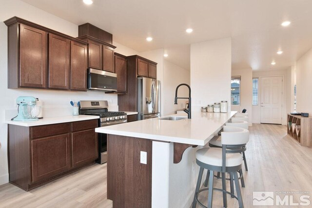 kitchen with sink, dark brown cabinets, stainless steel appliances, a breakfast bar area, and light hardwood / wood-style floors