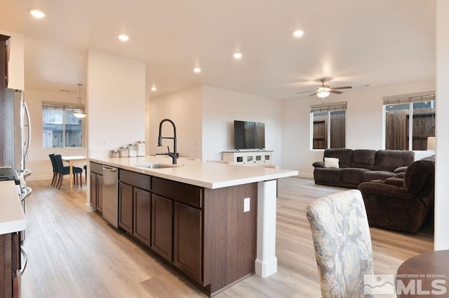 kitchen with ceiling fan, sink, dark brown cabinets, a kitchen island with sink, and light hardwood / wood-style flooring