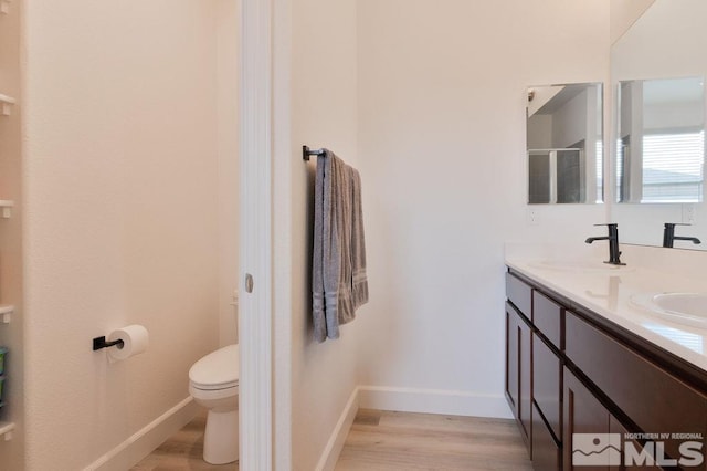 bathroom with wood-type flooring, vanity, toilet, and a shower with door