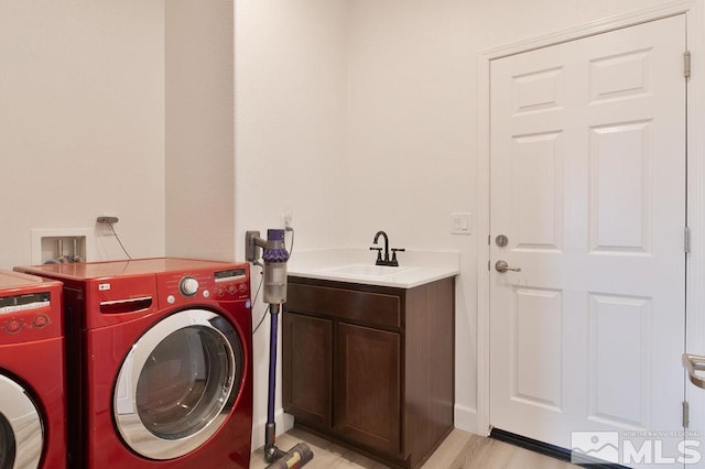 laundry room featuring washer and clothes dryer, cabinets, sink, and light hardwood / wood-style floors