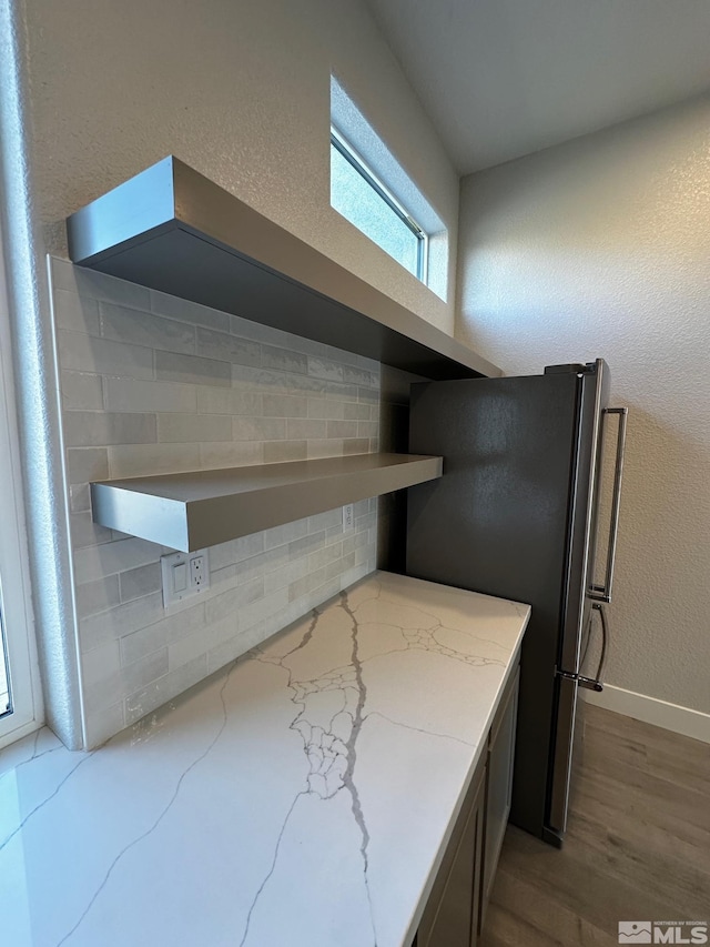 kitchen with decorative backsplash, stainless steel fridge, light stone countertops, and dark hardwood / wood-style flooring