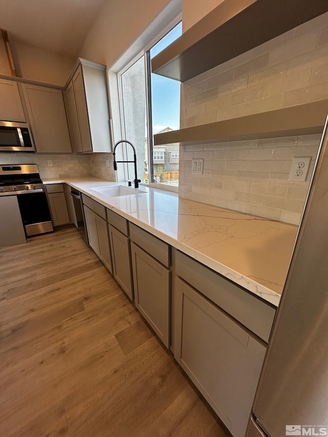 kitchen featuring light wood-type flooring, light stone counters, sink, decorative backsplash, and stainless steel appliances