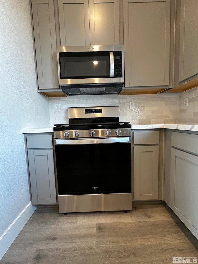 kitchen with appliances with stainless steel finishes, backsplash, light hardwood / wood-style floors, and gray cabinets