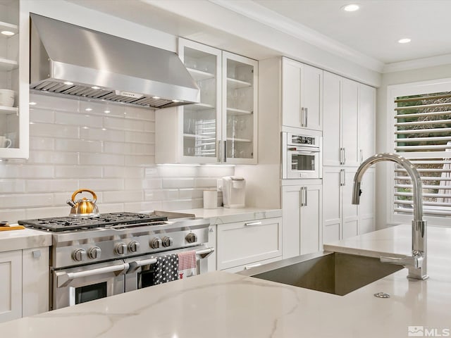 kitchen with light stone counters, white oven, white cabinets, wall chimney range hood, and high end range