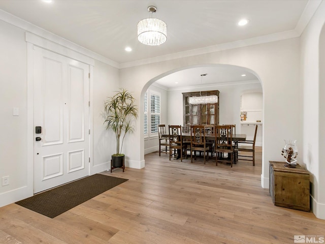 foyer entrance featuring ornamental molding, light wood-type flooring, and a chandelier