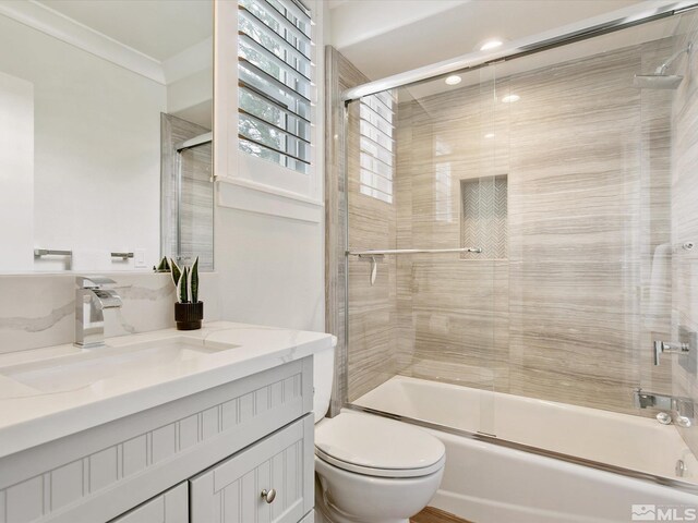 full bathroom featuring bath / shower combo with glass door, vanity, crown molding, and toilet