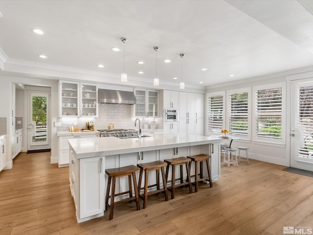 kitchen with pendant lighting, light wood-type flooring, white cabinets, wall chimney range hood, and a spacious island