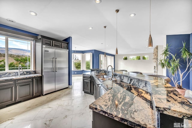 kitchen featuring stainless steel built in fridge, a large island, sink, and a wealth of natural light