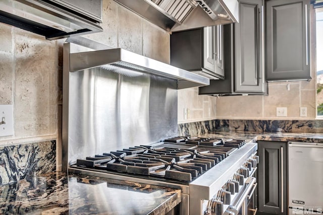 kitchen featuring gray cabinetry, stainless steel appliances, backsplash, and dark stone countertops