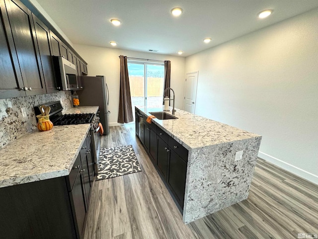 kitchen featuring appliances with stainless steel finishes, backsplash, a kitchen island with sink, and sink