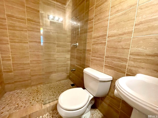 bathroom with tile walls, tiled shower, toilet, and sink