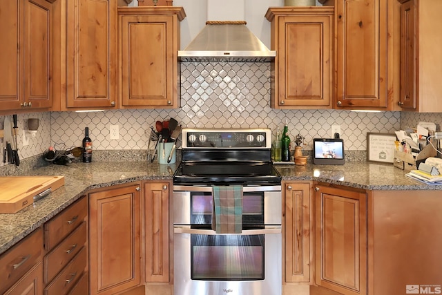 kitchen featuring wall chimney range hood, light stone countertops, stainless steel range with electric cooktop, and tasteful backsplash