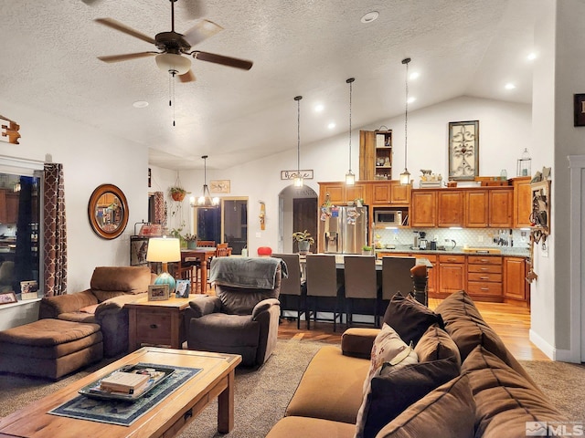 living room featuring ceiling fan with notable chandelier, vaulted ceiling, light hardwood / wood-style floors, and a textured ceiling