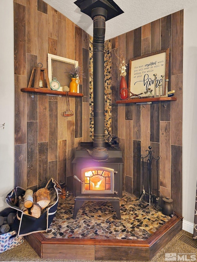 interior details featuring a wood stove, a textured ceiling, and wooden walls