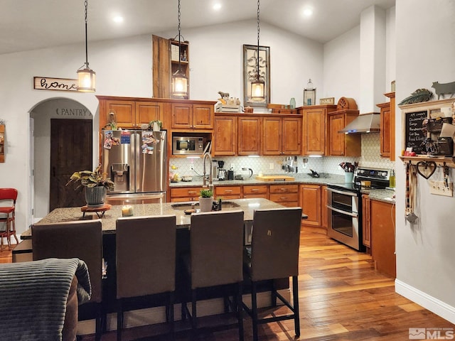 kitchen featuring pendant lighting, tasteful backsplash, a kitchen island with sink, appliances with stainless steel finishes, and light hardwood / wood-style floors