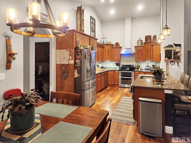 kitchen featuring light hardwood / wood-style floors, decorative light fixtures, wall chimney range hood, stainless steel appliances, and vaulted ceiling