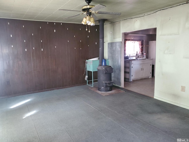 unfurnished room featuring wood walls, sink, ceiling fan, and a wood stove