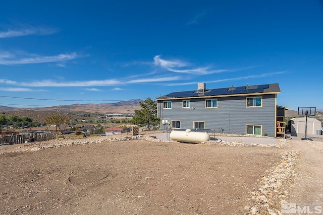 rear view of property featuring a mountain view, solar panels, and a shed