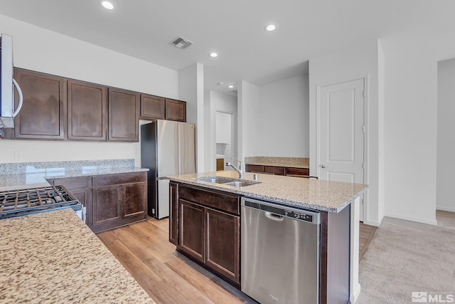 kitchen with dark brown cabinets, a kitchen island with sink, sink, light hardwood / wood-style flooring, and appliances with stainless steel finishes