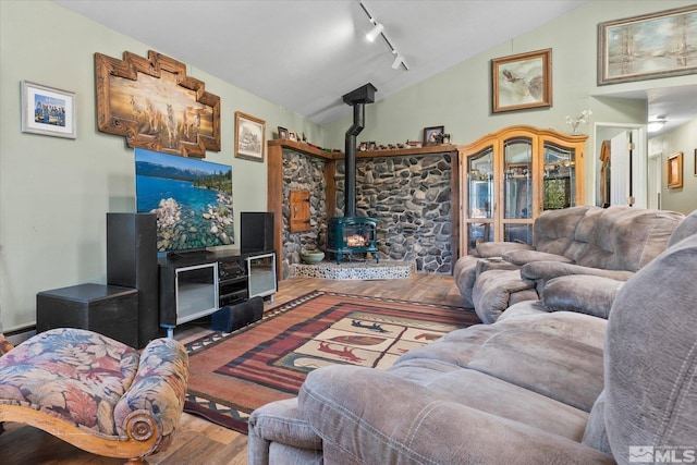 living room featuring wood-type flooring, vaulted ceiling, track lighting, and a wood stove