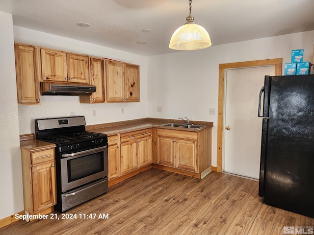 kitchen with hanging light fixtures, black refrigerator, light hardwood / wood-style flooring, gas stove, and sink