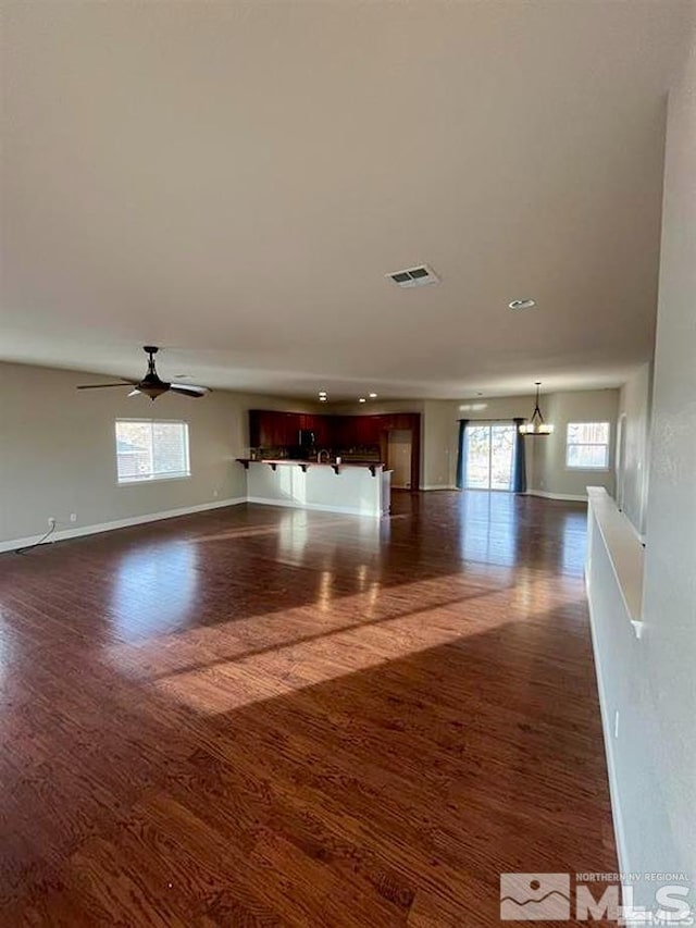 unfurnished room featuring dark hardwood / wood-style floors, ceiling fan with notable chandelier, and plenty of natural light