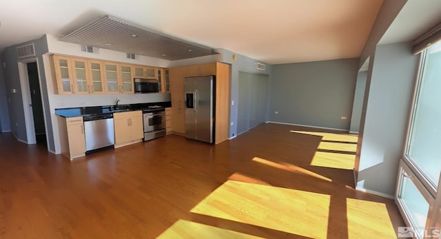 kitchen with appliances with stainless steel finishes, dark wood-type flooring, a sink, baseboards, and glass insert cabinets