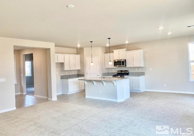 kitchen with white cabinetry, a breakfast bar, stainless steel appliances, a kitchen island with sink, and light carpet