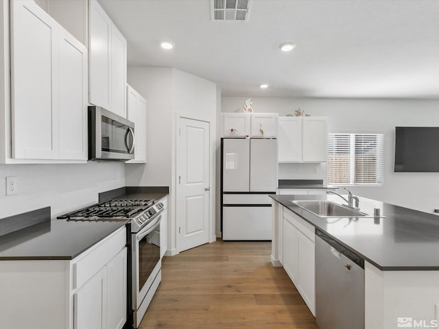 kitchen with dark countertops, wood finished floors, a sink, stainless steel appliances, and visible vents