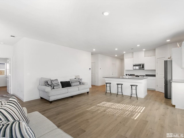 living area with recessed lighting, visible vents, light wood finished floors, and baseboards