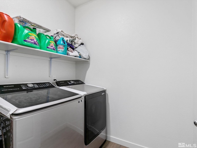 clothes washing area with washing machine and dryer, baseboards, wood finished floors, and laundry area