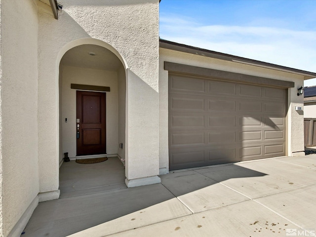 property entrance featuring a garage, driveway, and stucco siding