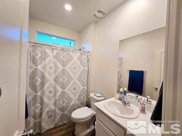 bathroom with a shower with shower curtain, hardwood / wood-style flooring, vanity, and toilet