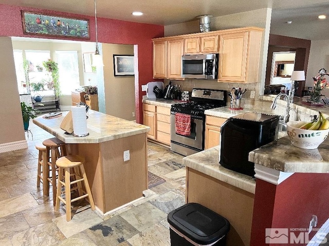 kitchen featuring a breakfast bar area, stainless steel appliances, decorative light fixtures, kitchen peninsula, and light brown cabinets