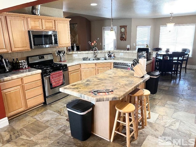 kitchen featuring sink, a center island, hanging light fixtures, light brown cabinets, and appliances with stainless steel finishes