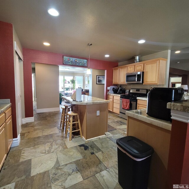 kitchen with light brown cabinetry, hanging light fixtures, a kitchen breakfast bar, a kitchen island, and stainless steel appliances