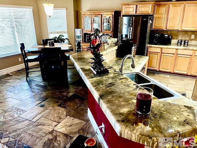 kitchen with pendant lighting, sink, decorative backsplash, a kitchen island with sink, and fridge with ice dispenser