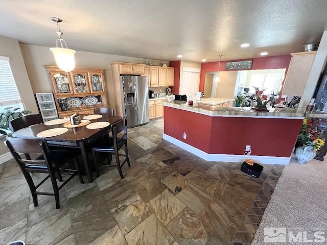 kitchen with a textured ceiling, pendant lighting, stainless steel fridge, and light brown cabinetry