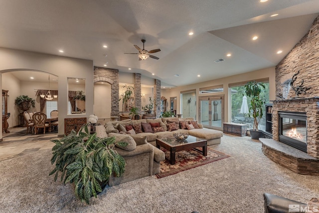 carpeted living room featuring ceiling fan with notable chandelier, a stone fireplace, and lofted ceiling