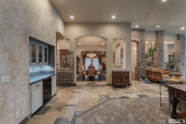 interior space featuring white cabinets, beverage cooler, a chandelier, a high ceiling, and dark stone countertops