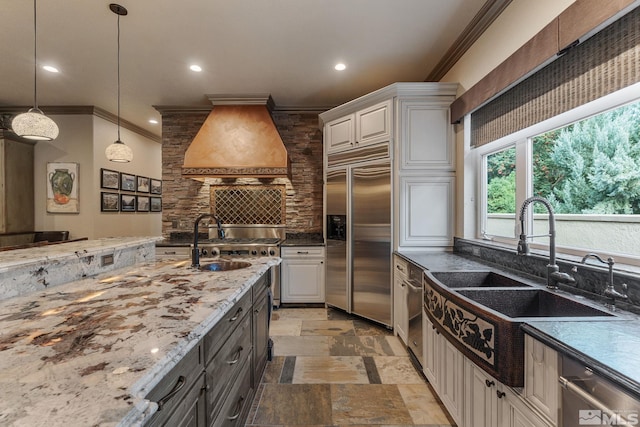 kitchen featuring sink, decorative light fixtures, white cabinetry, appliances with stainless steel finishes, and custom range hood