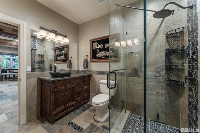 bathroom with tile walls, vanity, toilet, and a shower with door